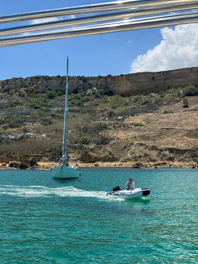 At anchor in turquoise water, the dinghy heading to shore.